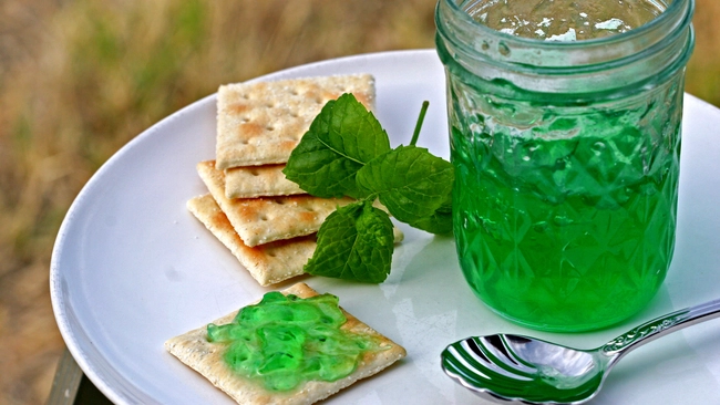 green mint jelly in a jar with crackers, a spoon, and a plate