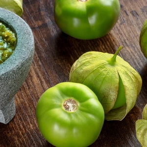 Green tomatoes next to a bowl of salsa verde