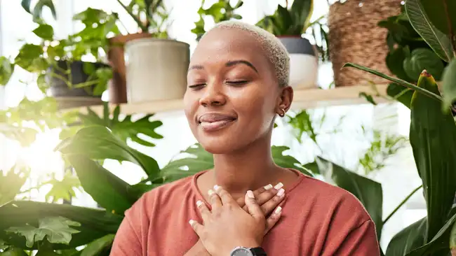 Balance, breathing and young woman by plants for zen meditation in a greenery nursery. Breathe, gratitude and young African female person with a relaxing peace mindset by an indoor greenhouse garden.